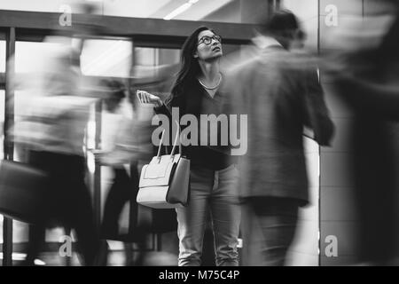 Asian businesswoman waiting for someone with people rushing in the lobby. Motion blur effect. Black and white shot. Stock Photo