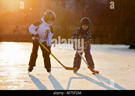 Children, boys, friends and brothers playing hockey and skating in the park on frozen lake, wintertime on sunset Stock Photo