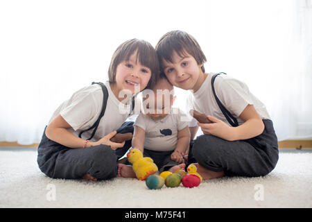 Three cute boys, siblings, brothers, playing with Easter eggs, eating chocolate bunnies at home, sunny living room Stock Photo