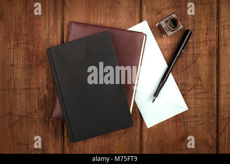 A black book, a leather journal, a blue envelope, and an ink well and pen Stock Photo