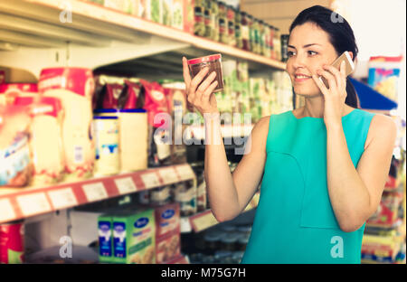 Woman choosing chocolate paste and talking on the phone in the supermarket Stock Photo