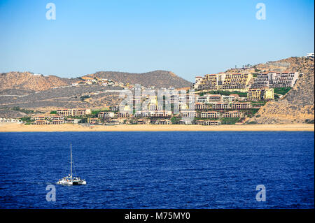 View from the sea to the coastline and beach (Playa El Medano), Cabo San Lucas. Colourful resort hotels, dry hilly backdrop & clear blue sky landscape Stock Photo