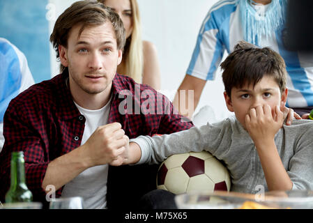 Father and son holding hands while watching football match at home Stock Photo