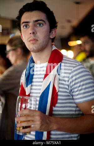British football fan watching match in bar with flag draped around neck Stock Photo