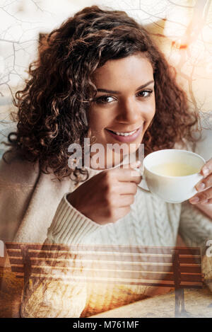 Beautiful young woman smiling cheerfully while drinking her tea Stock Photo