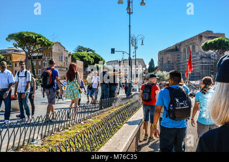 Italian policemen point across the road in front of tourists on the Via dei Fori Imperiali in Rome Italy with the Roman Colosseum and the Forum behind Stock Photo