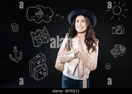 Smiling woman pressing her hands while dreaming about travelling Stock Photo