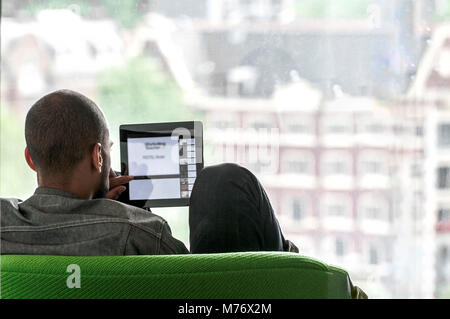 man sitting on a green bench looks at a small screen Stock Photo