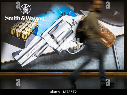 09 March 2018, Germany, Nuremberg: A visitor passes a poster by the American manufacturer Smith & Wesson (S&W) at the IWA OutdoorClassics trade show for hunting, shooting sports, equipment for outdoor activities and for civilian and official security applications. Photo: Daniel Karmann/dpa Stock Photo