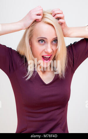 Confused surprised young blonde woman holding her head with two hands on white background. Stock Photo