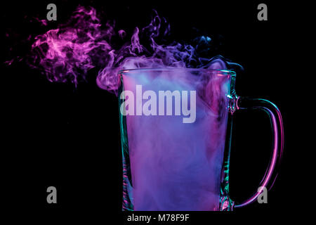 A glass transparent beer glass filled with a wig from a blue, blue, purple wipe smokes and stands on a black isolated background Stock Photo
