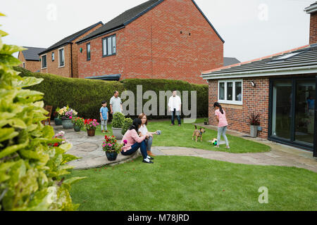 Family are relaxing in their garden in summer. The children are playing ball games with their father and grandfather. The mother and grandmother are t Stock Photo