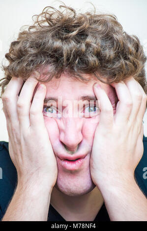Portrait of young shocked concentrated man that covers his depressed face with two hands on white background. Stock Photo