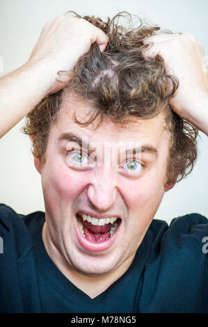 Portrait of young angry screaming curly man tears his hair out on white background. Stock Photo