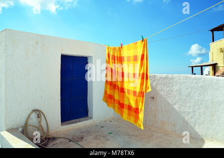 Pyrgos, Santorini / Greece - March 7, 2011: An orange and yellow bedspread, hanging to dry on a rooftop in the village of Pyrgos, Santorini, Greece Stock Photo