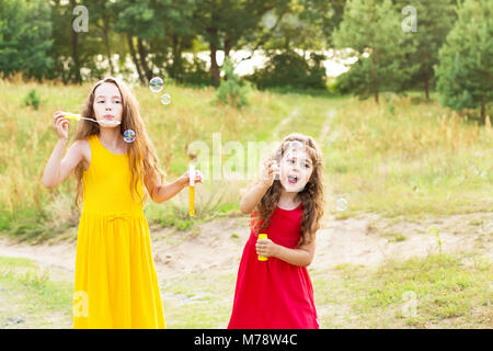 Two Cute Little Girsl blowing soap bubbles outdoor at sanny  summer day - happy childhood Stock Photo