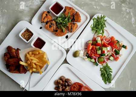 Nice table in the restaurant.Hearty and tasty lunch consisting of cheese Camembert in batter, Greek salad and grilled vegetables Stock Photo