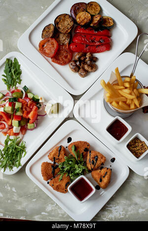 Nice table in the restaurant.Hearty and tasty lunch consisting of cheese Camembert in batter, Greek salad and grilled vegetables Stock Photo