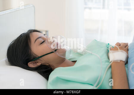 Asian young woman patient receiving oxygen mask lying on a hospital bed. Stock Photo