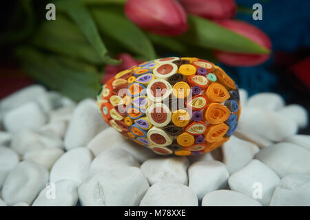 Hand-crafted Easter egg on the surface of white stones near of red tulips. Easter decor, selective focus. Stock Photo