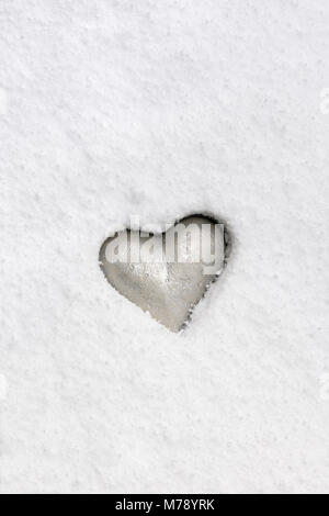 Silvery heart grey emedded in pristine snow. Stock Photo