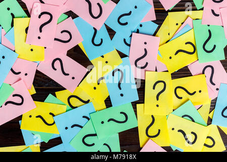 Too Many Questions on wooden background. Pile of colorful paper notes with question marks. top view. Stock Photo