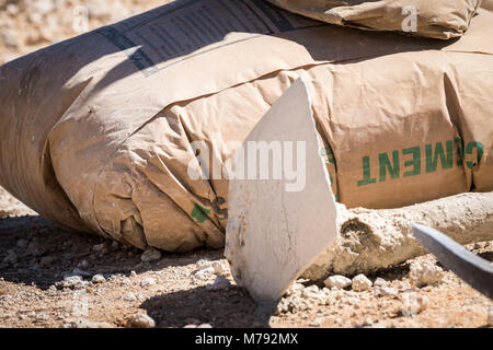 Tools and material used on a Construction Site. Bag of Cement, hoe and pickaxe on the ground outside used by construction workers on hot sunny day. Stock Photo