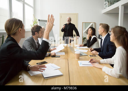 Businesswoman raising hand asking senior coach questions at team Stock Photo