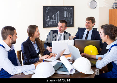 Cheerful young team architectural engineers discussing business project and smiling indoors Stock Photo