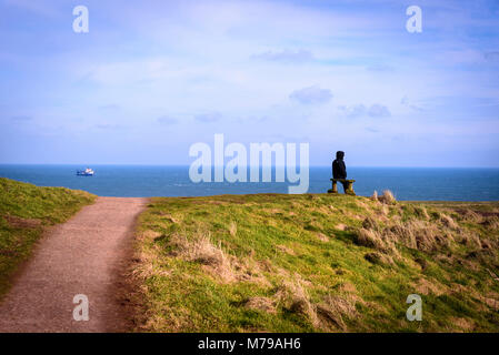 Lone man sitting on bench looking out to sea Stock Photo