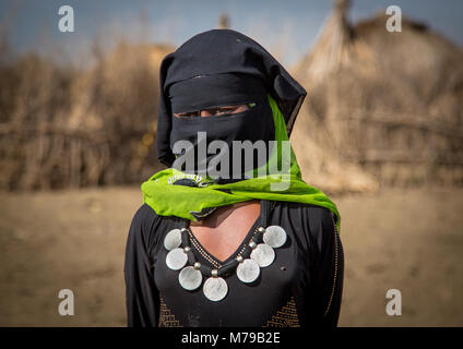 Portrait of an oromo veiled woman with a silver thalers necklace standing in front of her village, Amhara region, Artuma, Ethiopia Stock Photo