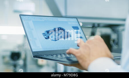Close-up of the Engineer Holding Laptop with CAD Component Model on Screen. In the Background Modern Factory Equipment. Stock Photo