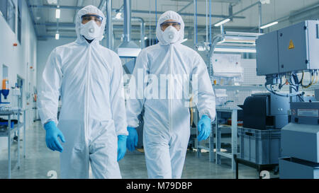 Two Engineers/ Scientists in Hazmat Sterile Suits Walking Through Technologically Advanced Factory/ Laboratory. Clean High-Tech Environment with CNC Stock Photo