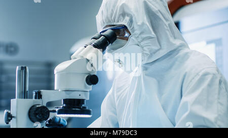 Close-up of the Engineer/ Technician/ Scientist Checking Component under the Microscope. He Wears Sterile Coverall Suit and Protective Glasses Stock Photo