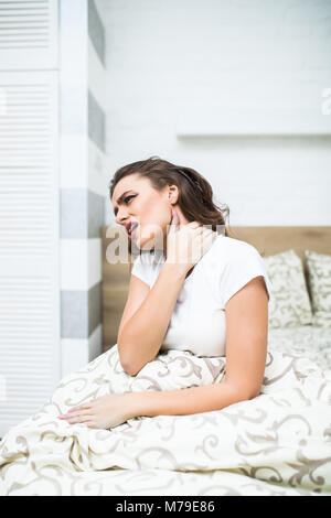 Young woman sitting on the bed with pain in neck Stock Photo