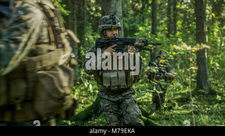 Squad of Five Fully Equipped Soldiers in Camouflage on a Reconnaissance Military Mission, Rifles in Firing Position. They're Moving Through Forest. Stock Photo