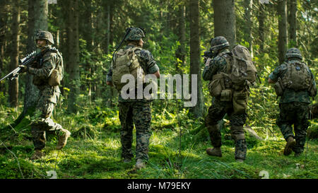 Squad of Five Fully Equipped Soldiers in Camouflage on a Reconnaissance Military Mission, Rifles in Firing Position. They're Moving Through Forest. Stock Photo