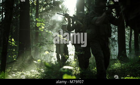 Squad of Five Fully Equipped Soldiers in Camouflage on a Reconnaissance Military Mission, Rifles Ready to Shoot. They're Moving Through Forest. Stock Photo