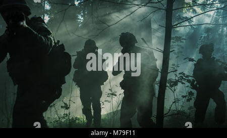 Squad of Five Fully Equipped Soldiers in Camouflage on a Reconnaissance Military Mission, Rifles Ready to Shoot. They're Moving Through Forest. Stock Photo