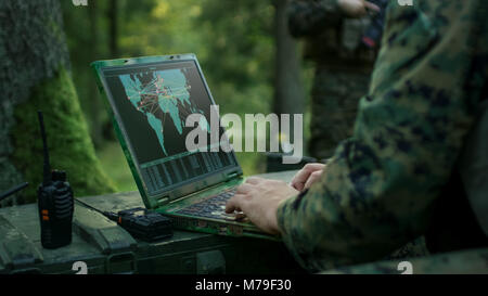 Military Operation in Action, Soldiers Using Military Grade Laptop Targeting Enemy with Satellite. In the Background Camouflaged Tent on the Forest. Stock Photo