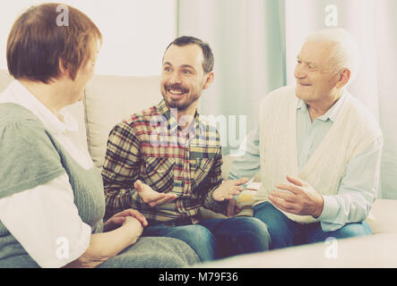 Elderly grandparents friendly conversation with grandson sitting on sofa Stock Photo