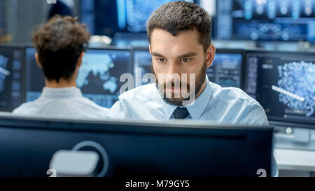 Neural Network and Machine Learning Engineer Programming at His Workstation. Office is Crowded With People Working. Multiple Displays Show Info Stock Photo