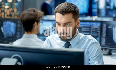 Neural Network and Machine Learning Engineer Programming at His Workstation. Office is Crowded With People Working. Multiple Displays Show Info Stock Photo