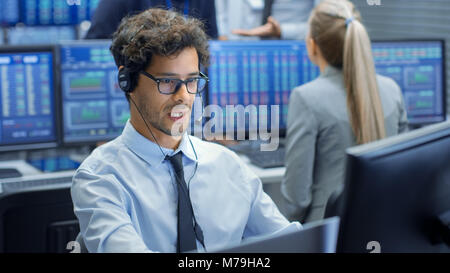 Stock Trader Making Sales with a Headset. In the Background Stock Exchange Office and Group of Traders Working at their Workstations. Stock Photo