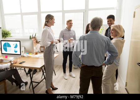 Smiling happy young and senior office workers talking in coworki Stock Photo