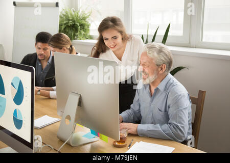 Smiling young manager helping senior worker with computer office Stock Photo