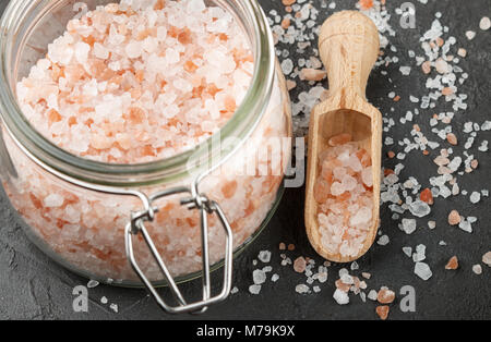 Himalayan pink salt in wooden spoon and jar on a black background. Selective focus Stock Photo