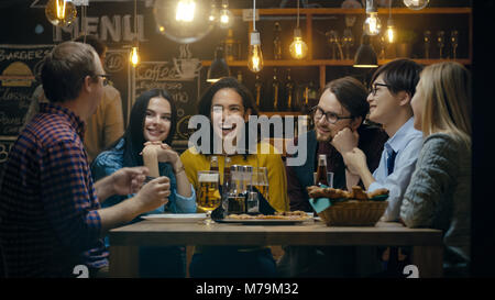 Diverse Group of Young People Have Fun in Bar, Have Conversation, Telling Stories and Jokes. They Drink Various Drinks. They're in the Stylish Hipster Stock Photo