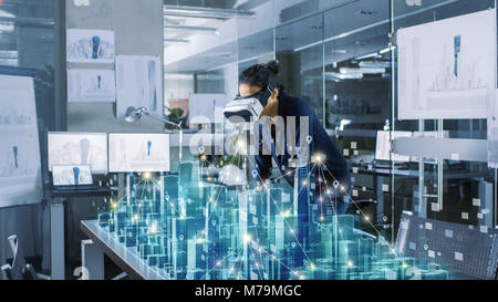 Professional Female Architect Wearing Makes Gestures with Augmented Reality Headset, Shows Statistics for 3D Model. High Tech Office Use VR Helmet Stock Photo