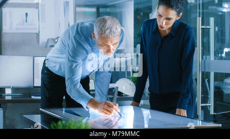 Senior Male and Young Female Architectural Designers Draw Building Concept on a GraphicsTablet Display Vertical Touchscreen Table. Stock Photo